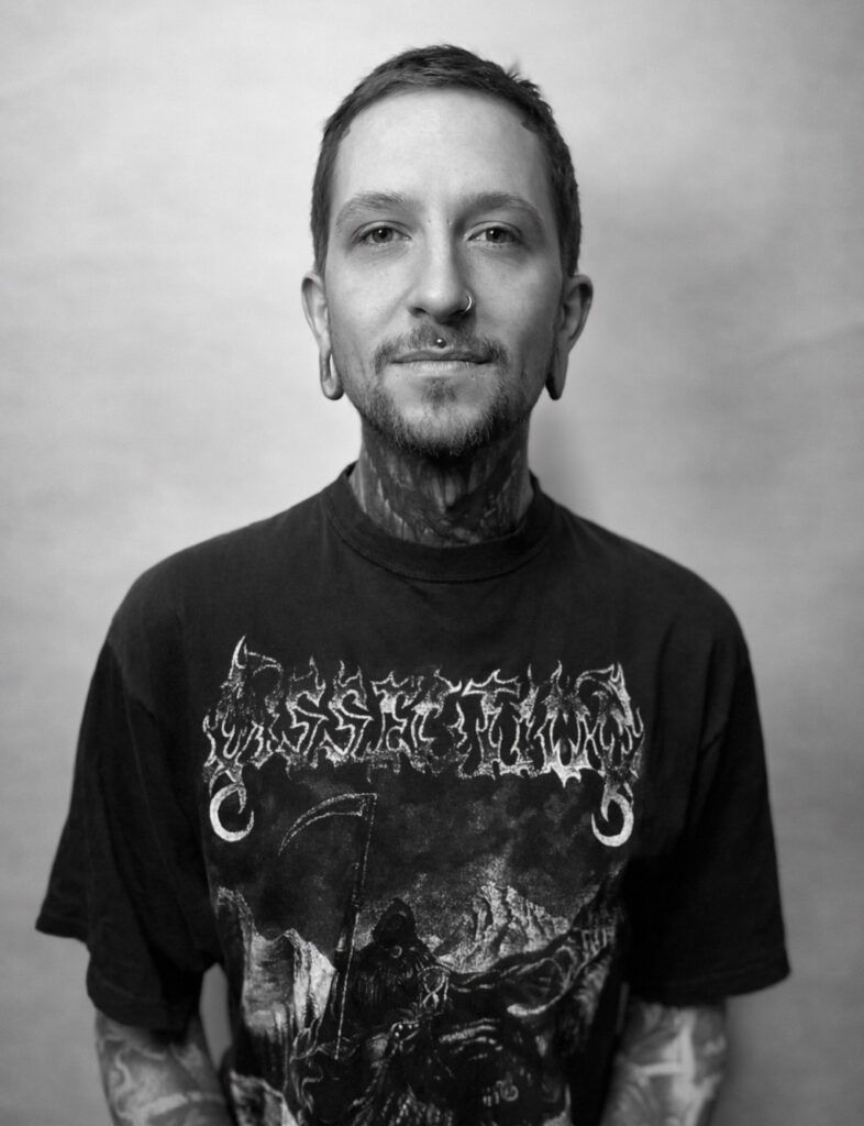 Junger Mann mit Tunneln in den Ohren und Nasenpiercing lacht freundlich in die Kamera